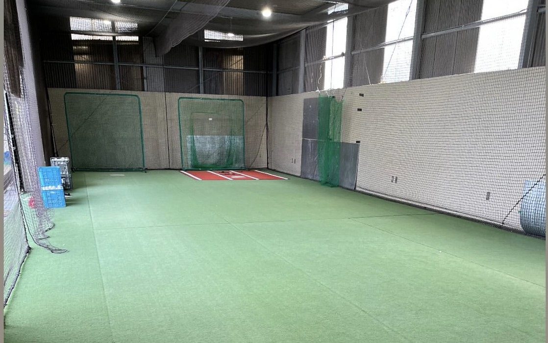 室内練習場の全景。人工芝の床の奥にホームベースと防球ネットが並ぶ